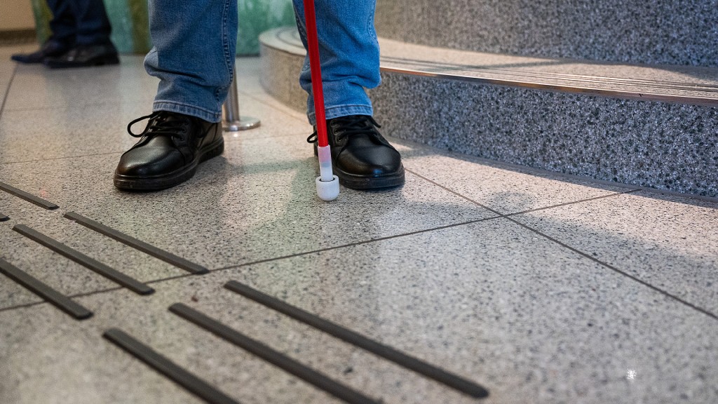 Eine blinde Person steht mit Langstock vor dem neu angebrachten Bodenleitsystem für blinde und seheingeschränkte Menschen.