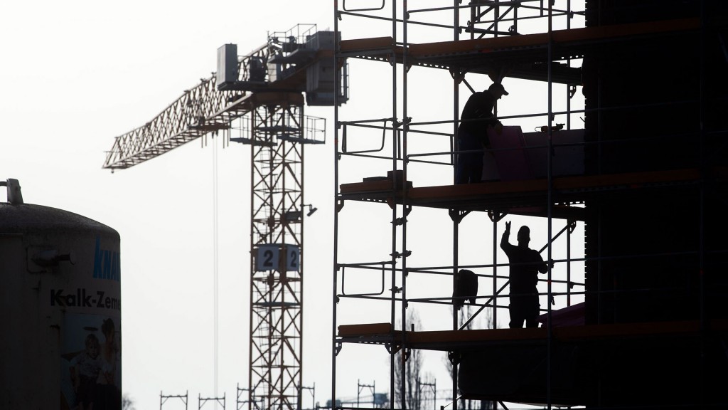 Foto: Bauarbeiter stehen auf einem Gerüst am Neubau eines Mehrfamilienhauses