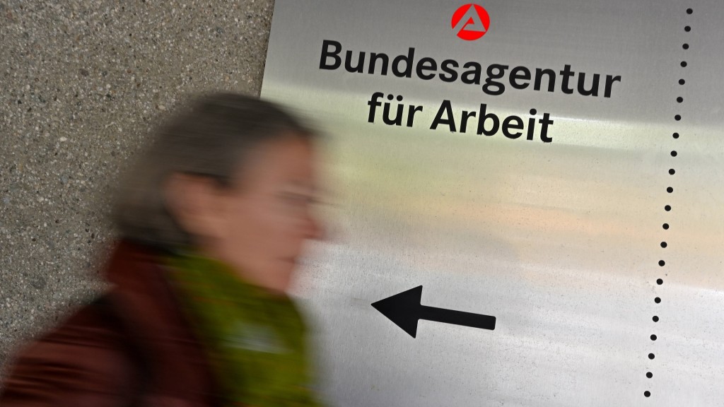 Eine Frau geht am Schild einer Arbeitsagentur vorbei.