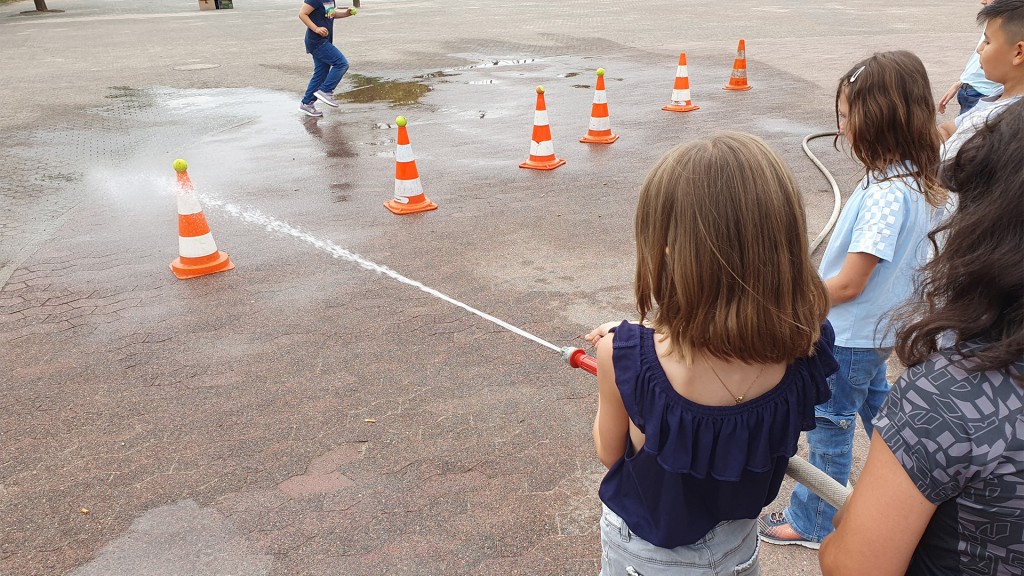 Kinder versuchen mit dem Wasserstrahl eines Feuerwehrschlauchs ein Ziel zu treffen