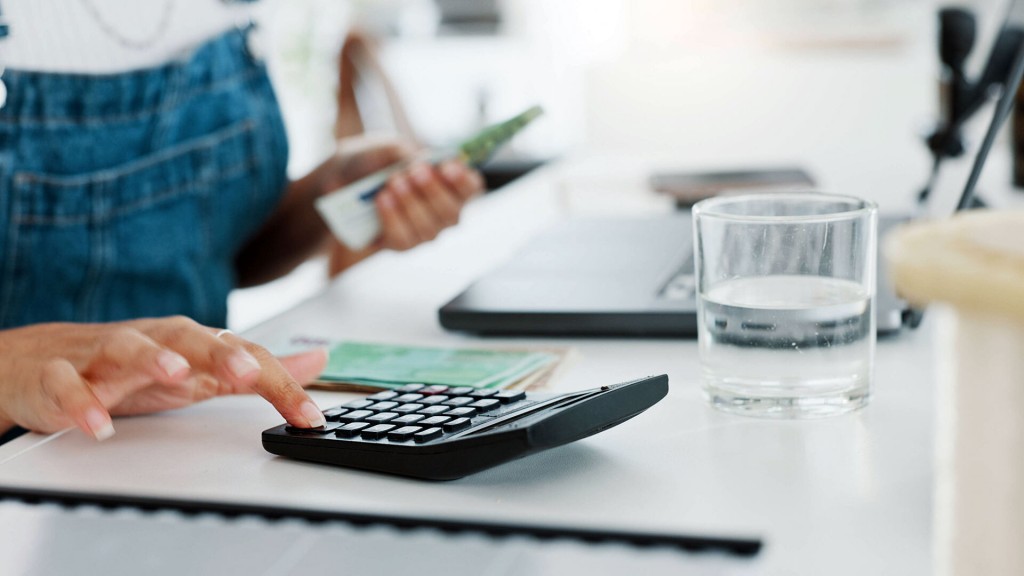 Foto: Eine Frau sitzt am Tisch mit Geldscheinen in der Hand und tippt auf einen Taschenrechner