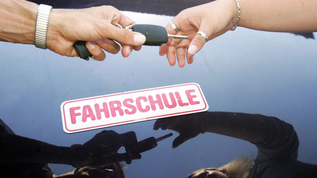 Ein Fahrlehrer überreicht seiner Fahrschülerin den Schlüssel zum Fahrzeug