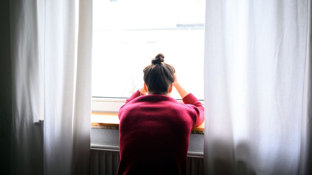 Eine Frau sitzt mit Kopf in den Händen am Fenster