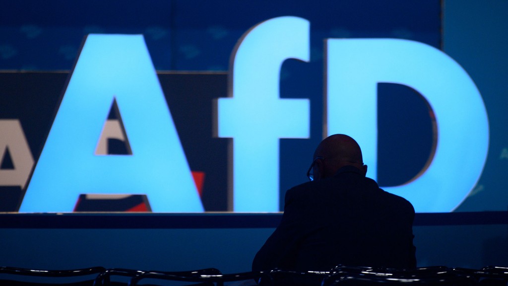 Foto: Eine Person sitzt alleine zwischen leeren Stühlen vor einem großen AfD-Logo