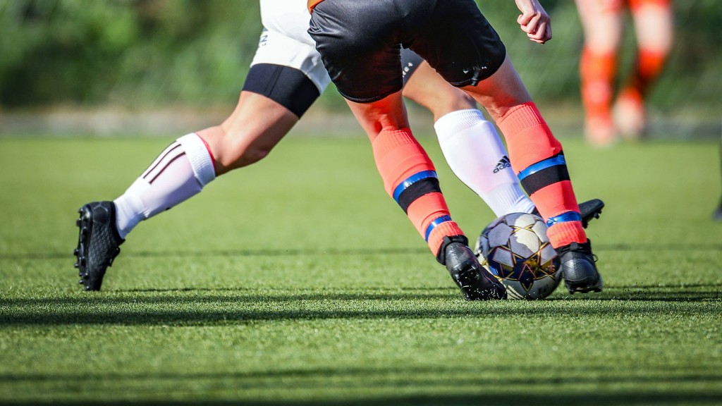 Nahaufnahme eines Fußball und Füße zweier Spieler im Zweikampf