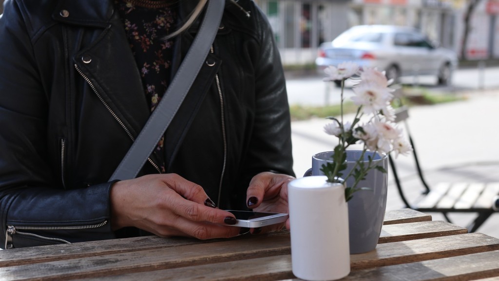 Eine Frau sitzt mit ihrem Handy draußen an einem Bistro Tisch.