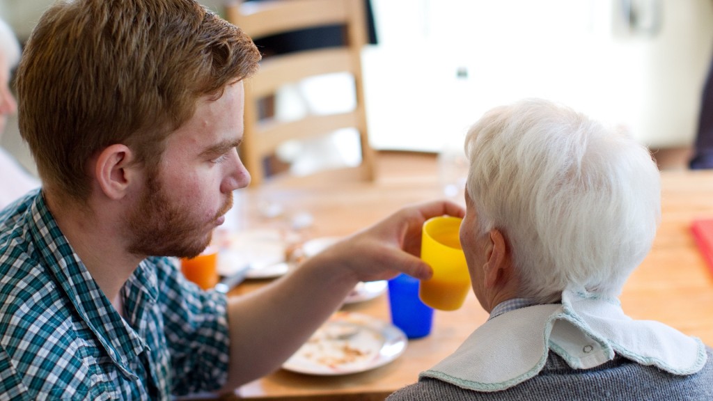 Ein junger Mann hilft einer Seniorin beim Einnehmen einer Mahlzeit