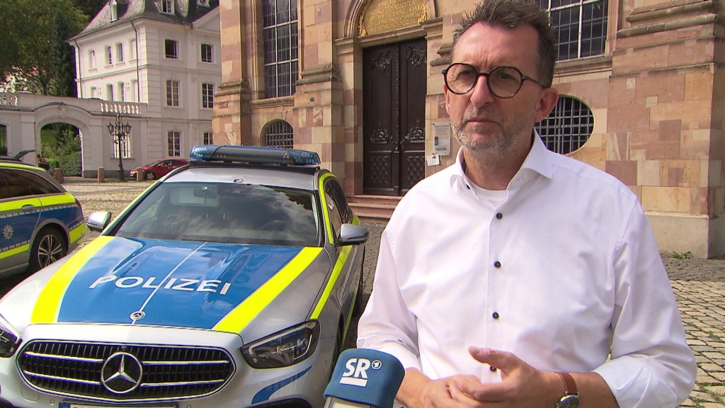 Innenminister Jost steht vor Polizeiwagen an der Ludwigskirche