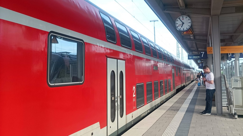 Fahrgäste stehen an einem Bahngleis vor einem Zug