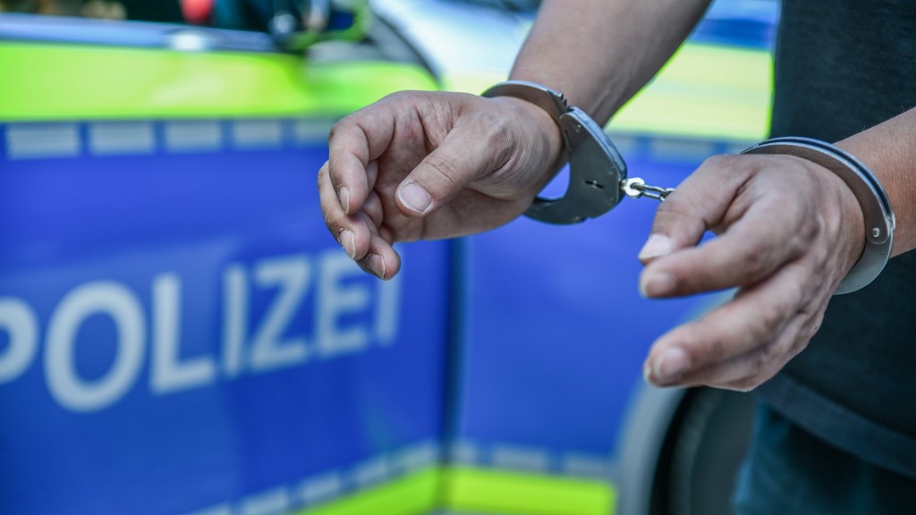 Eine Person mit Handschellen vor einem Polizeifahrzeug