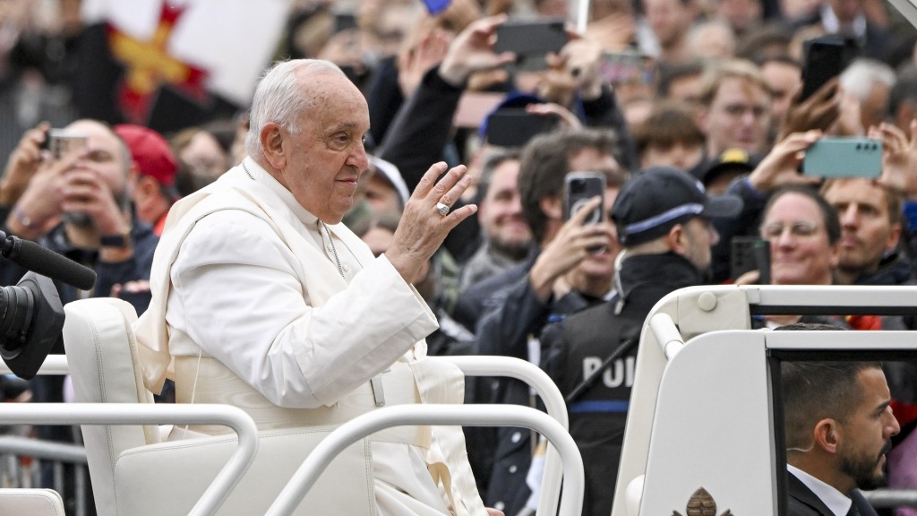 Papst Franziskus wink jubelnden Menschen aus dem Papamobil zu.