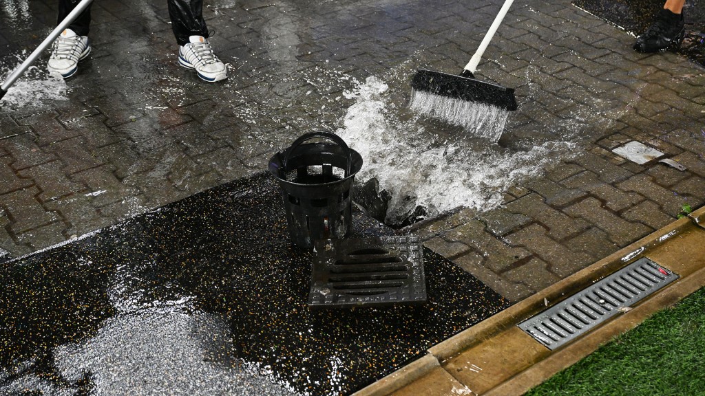 Foto: Zwei Helfer schieben Wasser in einen Bodenablauf nach einem heftigen Regenschauer