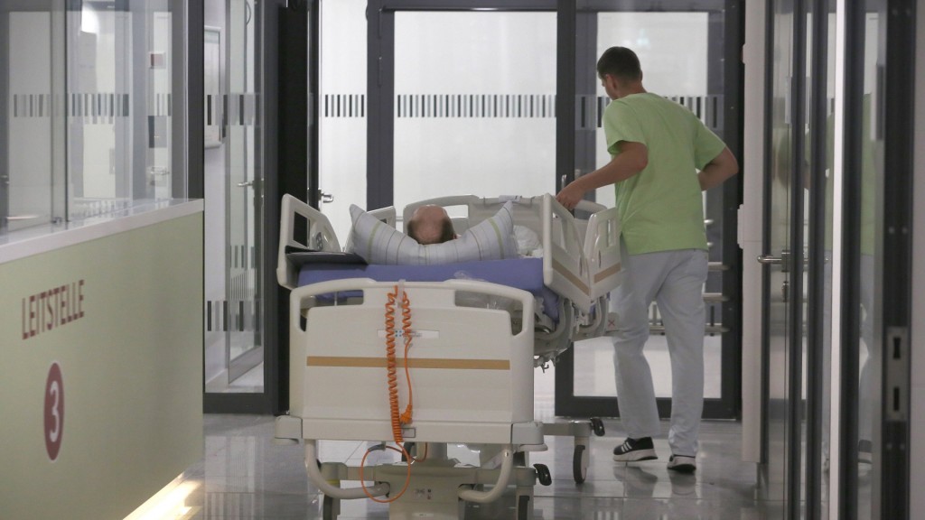 Ein Patient wird im Krankenbett von einem Pfleger über den Flur geschoben.