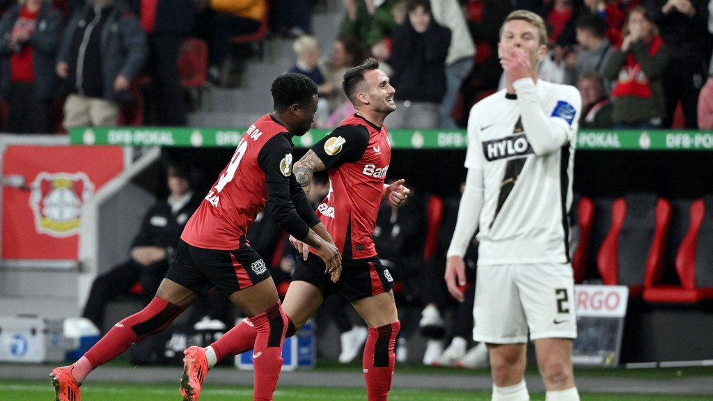 Foto: Aleix Garcia und Nathan Tella (Bayer 04 Leverkusen) laufen feiernd hinter Elias Baum (SV Elversberg) mit resigniertem Gesichtsausdruck