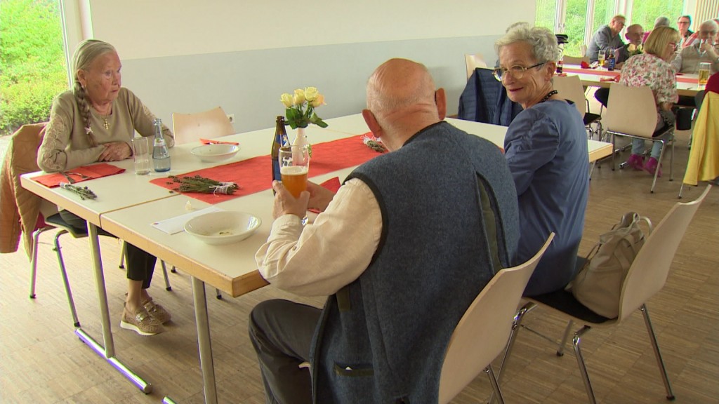 Mehrere Menschen, vor allem viele Senioren, sitzen an einem Tisch und unterhalten sich.