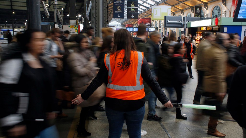 Eine SNCF-Mitarbeiterin in Warnweste weist französischen Bahnreisenden den Weg