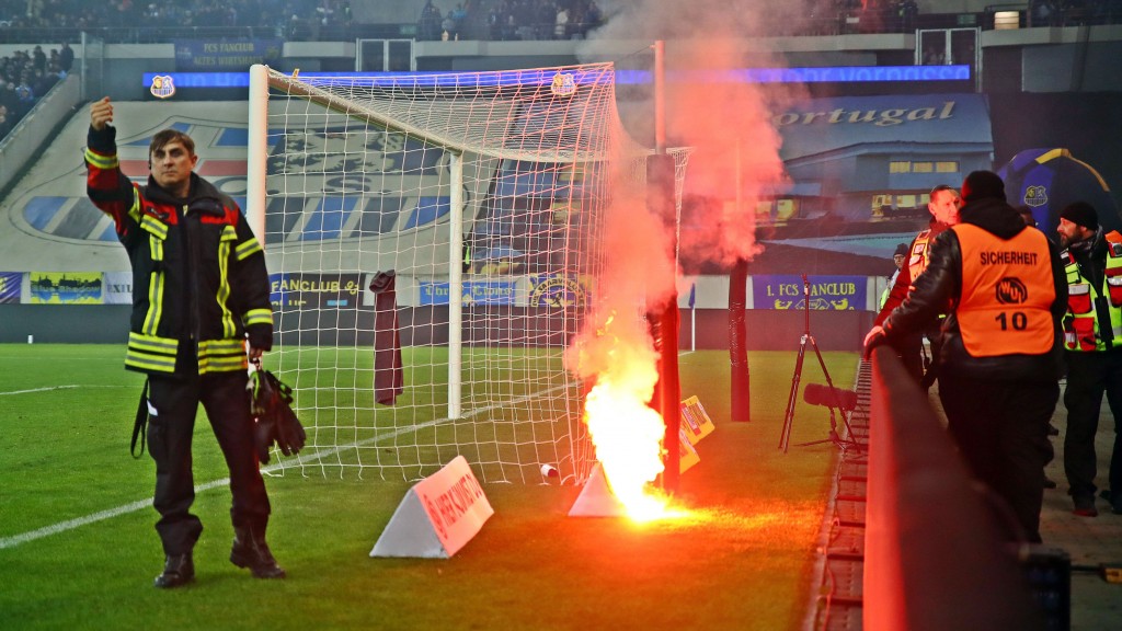 Beim Heimspiel des FC Saarbrücken gegen Rot-Weiß-Essen im Ludwigsparkstadion setzt eine Leuchtrakete aus dem Gästeblock ein Werbebanner am Spielfeldrand in Brand