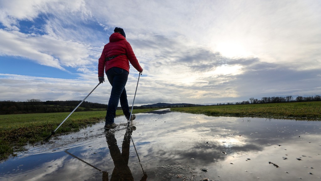 Eine Frau geht mit ihren Lauf-Stöcken durch eine große Regenpfütze am Feldrand