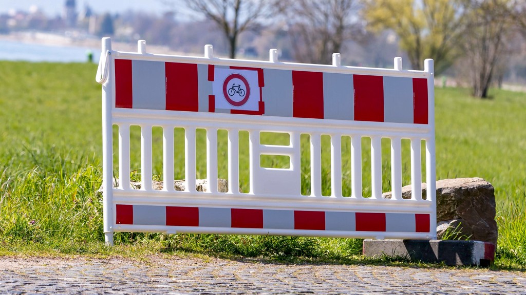 Eine Absperrbarke steht vor einem Fuß- und Radweg am Flussufer