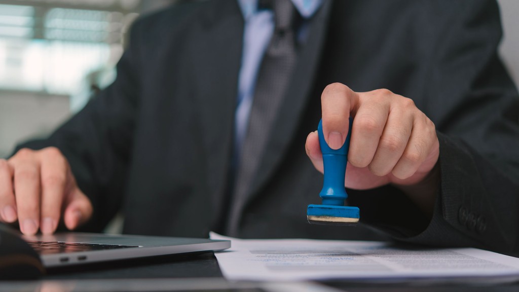 Foto: Ein Mann im Anzug sitzt am Schreibtisch mit einem Stempel in der Hand