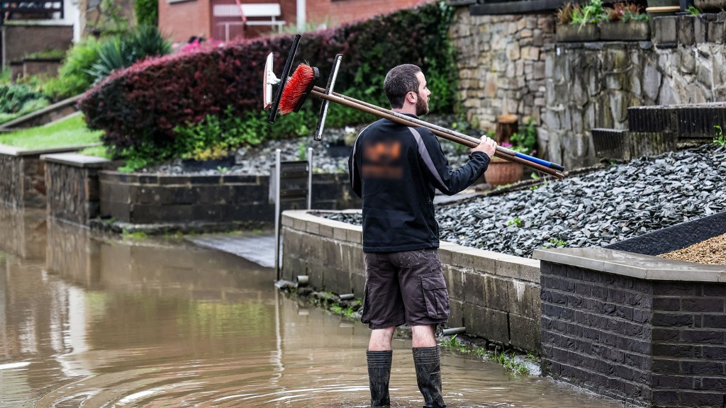 Ein Mann steht mit Gummistiefeln, Besen und Abziehern im Hochwasser