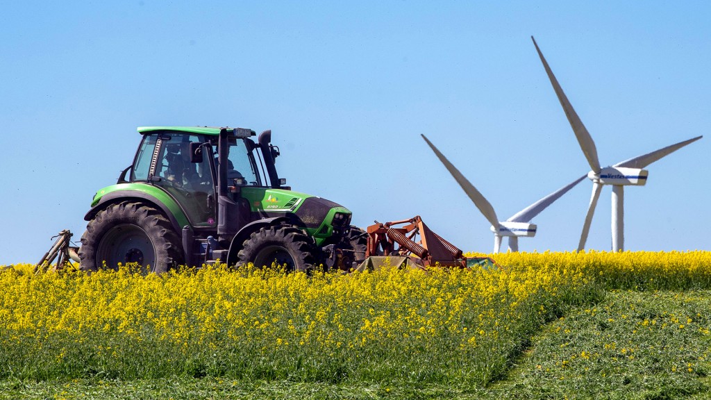 Ein Landwirt fährt vor einer Windkraftanlage mit einem Traktor über ein Rapsfeld