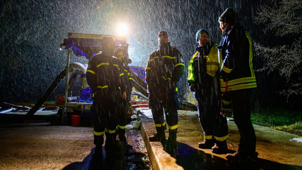 Foto: Einsatzkräfte von THW und Feuerwehr stehen bei Starkregen an einer Pumpe.