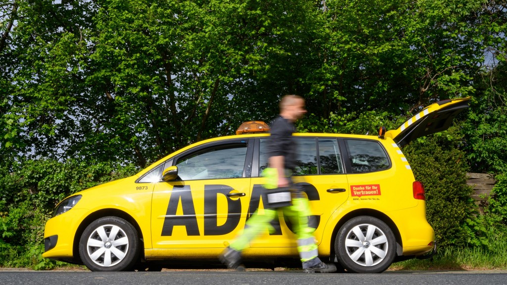 Ein Pannenhelfer vom ADAC geht an seinem Auto mit einer Autobatterie in der Hand vorbei. 
