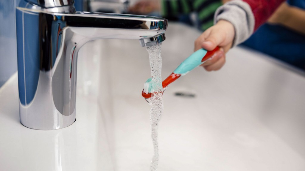 Ein Kind hält seine Zahnbürste unter einen laufenden Wasserhahn