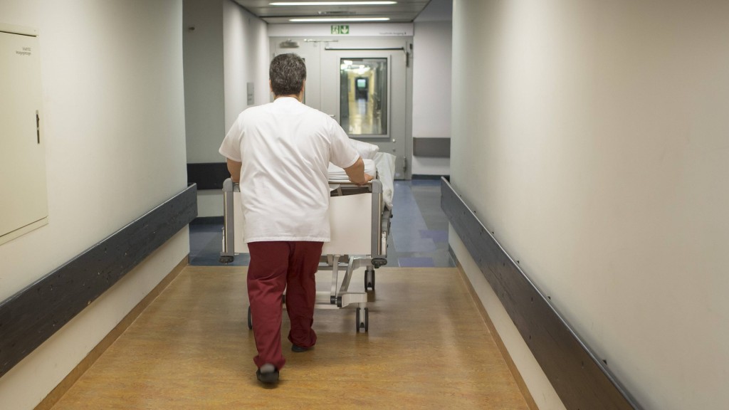 Foto: Ein Pfleger schiebt ein Bett durch einen Krankenhausflur.