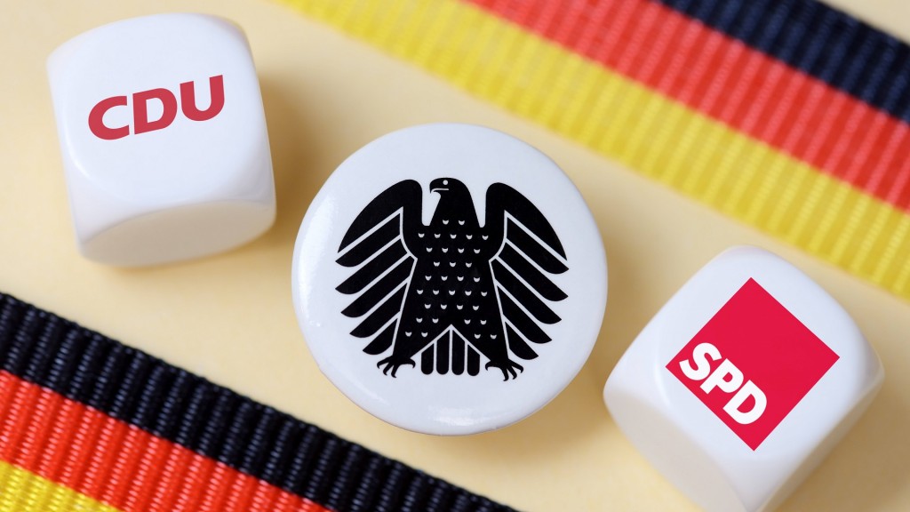 Würfel mit den Logos der CDU und SPD liegen auf einem Tisch. Dazwischen ein Sticker mit dem Bundesadler.