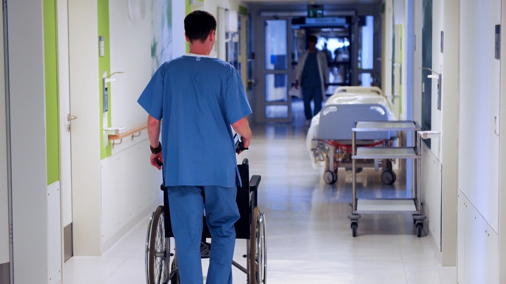 Ein Krankenpfleger schiebt einen Rollstuhl über den Krankenhausflur.