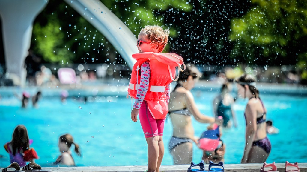 Ein kleines Kind steht mit Schwimmlernweste am Beckenrand im Freibad