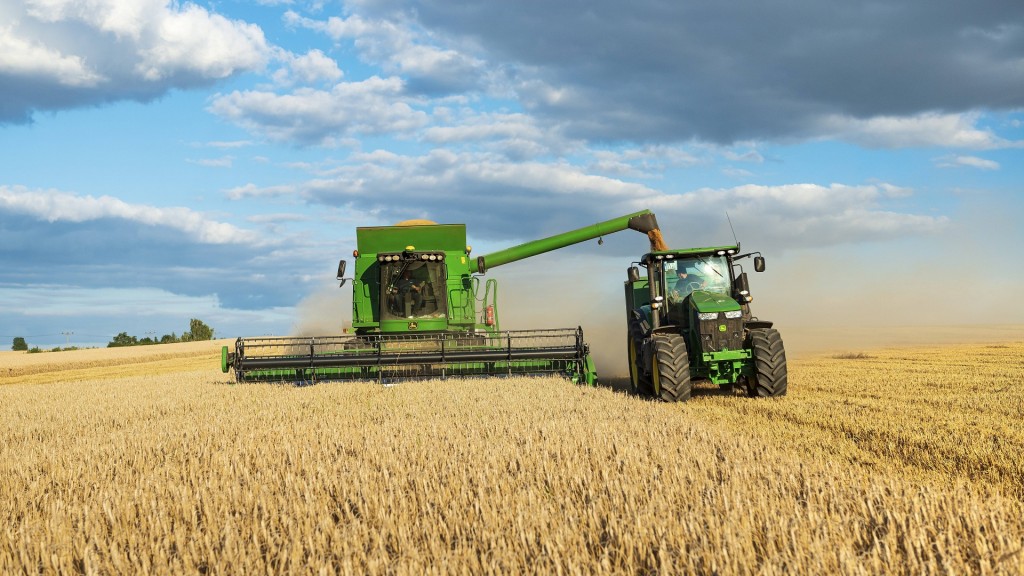 Mähdrescher erntet Weizen und entlädt Getreide auf einen Traktor mit Anhänger.