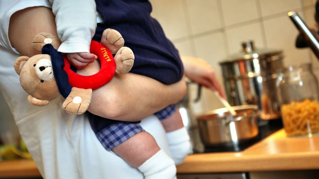 Eine Mutter hält beim Kochen ihr Kleinkind auf dem Arm.
