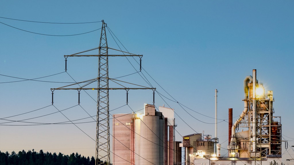 Strommasten stehen im Morgenlicht vor einer Industrieanlage