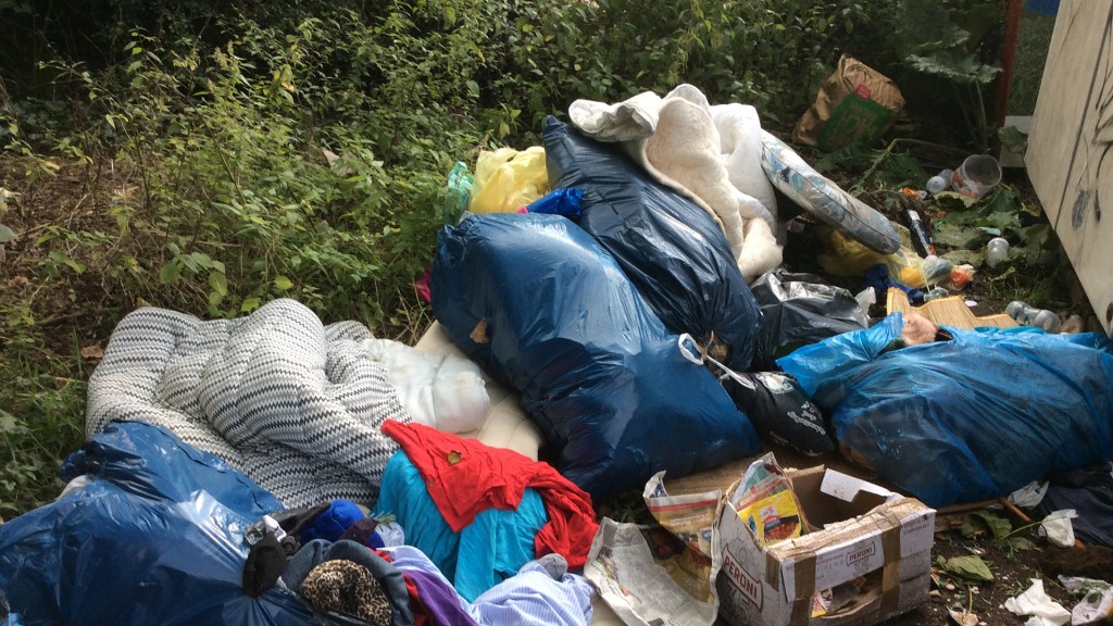 Foto: Kleidersäcke und Müll neben Containern