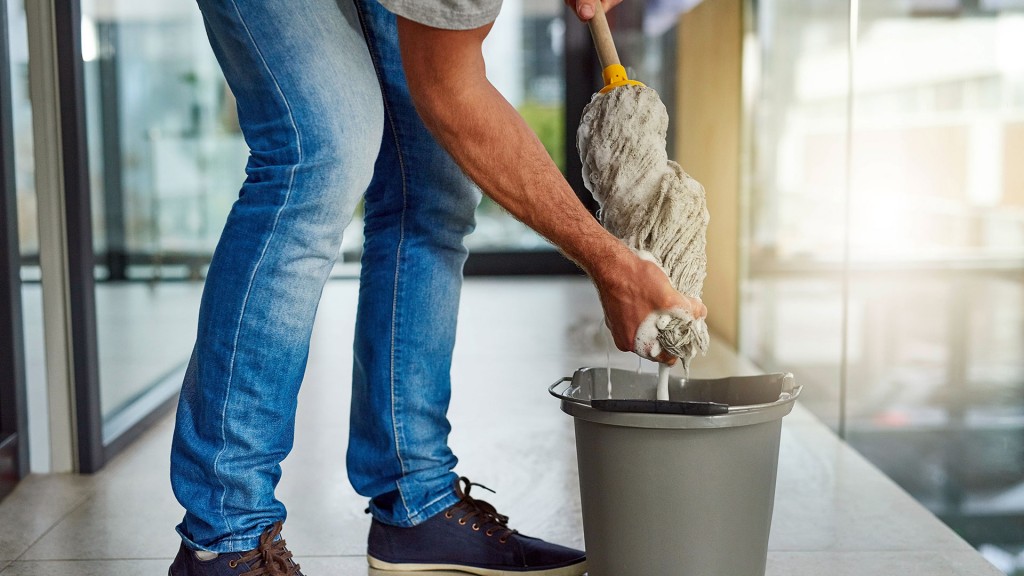 Foto: Ein Mann wringt einen Putzlappen über dem Eimer aus