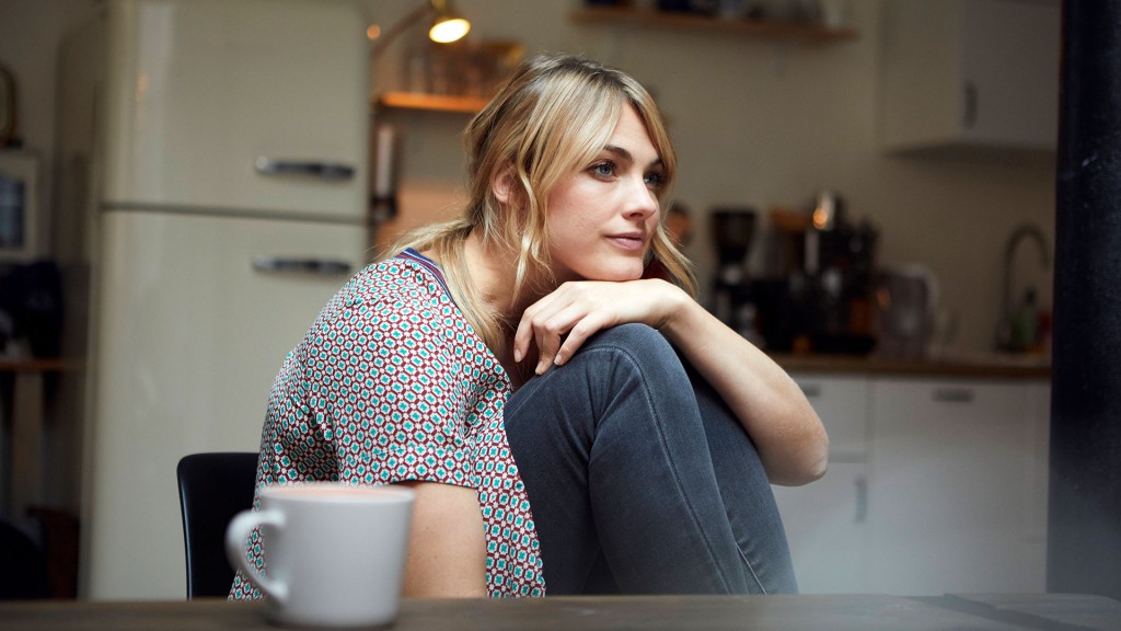 Eine junge Frau sitzt mit zufriedenem Gesichtsausdruck in ihrer Wohnung