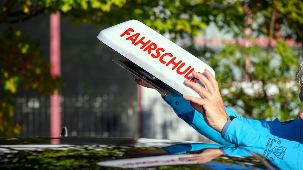 Ein Fahrlehrer hantiert mit dem Dachschild eines Fahrschulautos