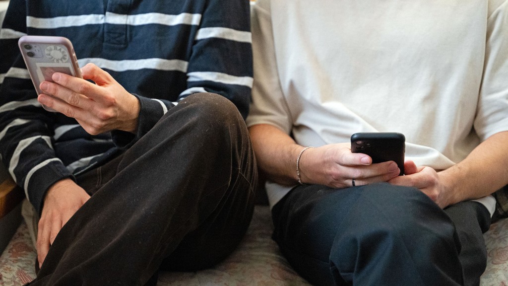 Zwei Personen sitzen nebeneinander auf einer Bank und halten ihr Smartphones in den Händen