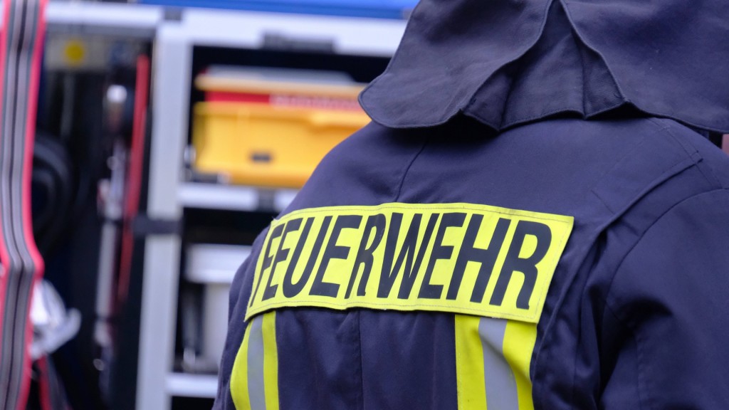 Symbolbild Feuerwehr. Ein Feuerwehrmann steht vor dem Einsatzwagen.