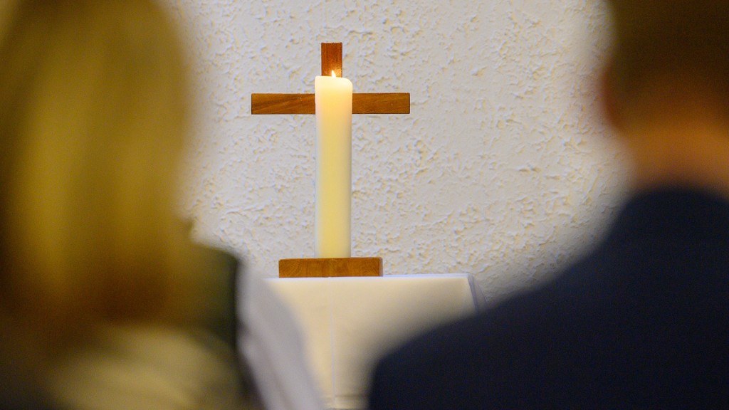 Foto: Eine Kerze brennt vor einem Kreuz