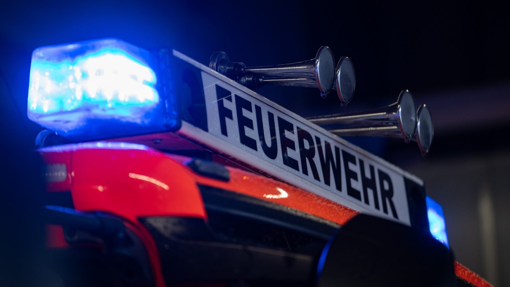 Foto: Ein Einsatzfahrzeug der Feuerwehr steht mit Blaulicht bei der FeuerwacheEin Fahrzeug der Feuerwehr steht bei einem Einsatz auf einer Straße, während im Vordergrund das Blaulicht eines Polizeifahrzeugs zu sehen ist