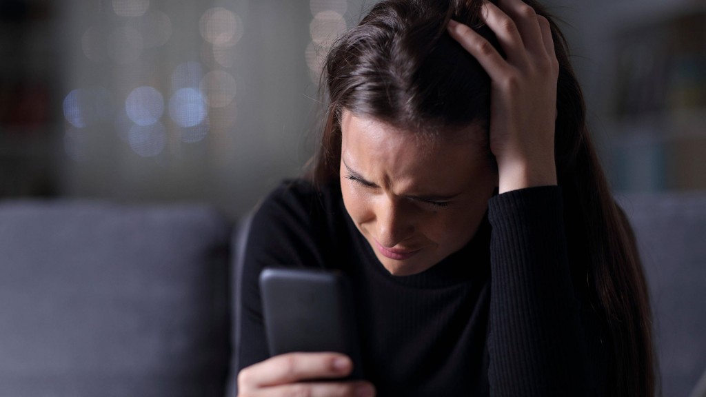 Eine junge Frau schaut verzweifelt auf ihr Smarphone