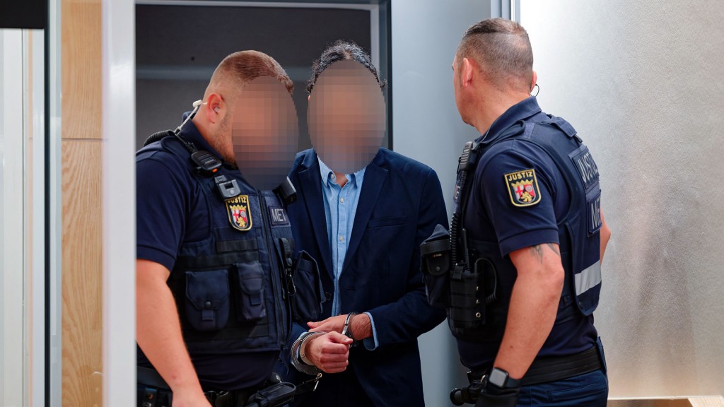 Der Angeklagte im Zugbegleiter-Mordprozess kommt in Begleitung von zwei Justizbeamten in den Verhandlungssaal des Landgerichts Zweibrücken