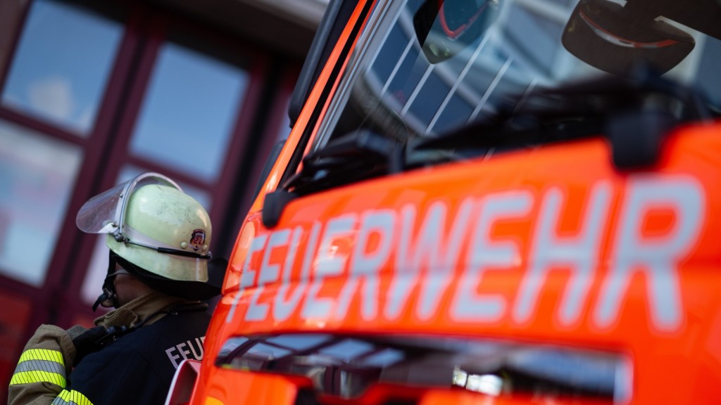 Foto:Eine Einsatzkraft der Feuerwehr steht neben einem Einsatzfahrzeug der Feuerwehr. 