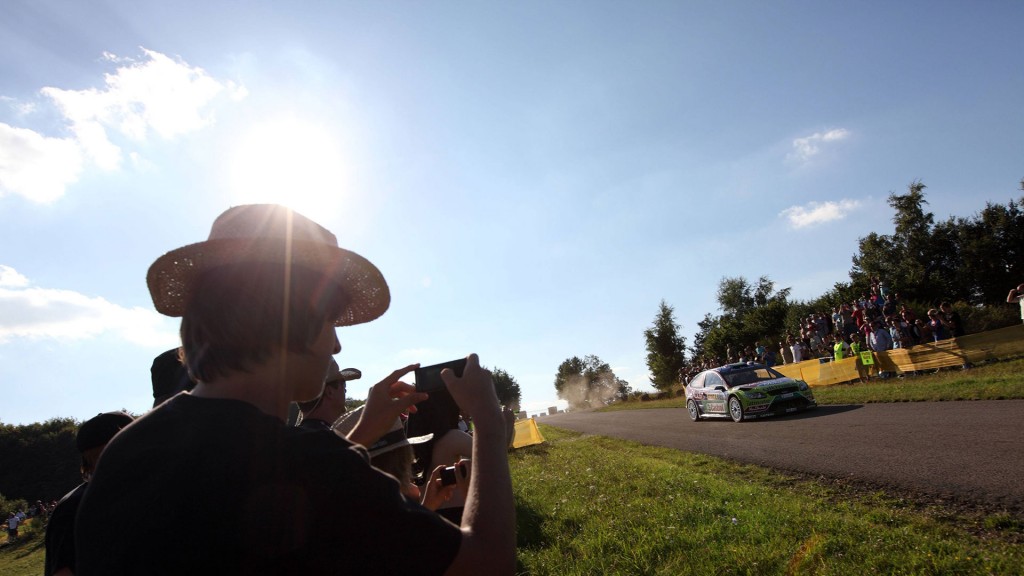 Zuschauer auf einem Feld, die die ADAC-Rallye verfolgen und filmen