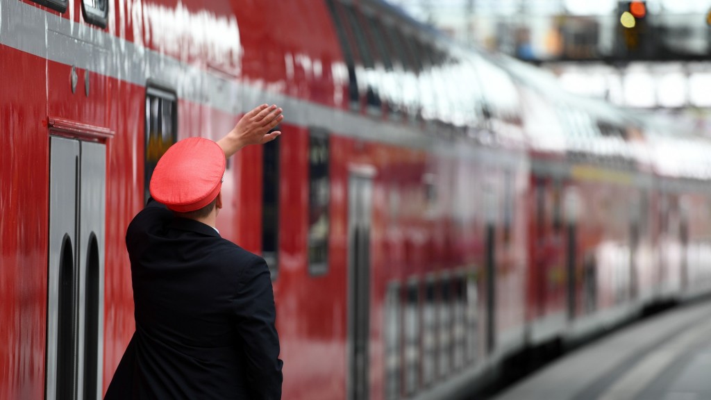 Foto: Ein Zugbegleiter steht neben einer Regionalbahn am Bahnsteig.