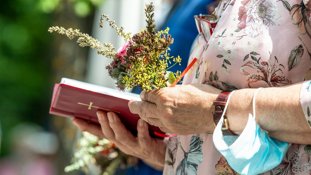 Eine Gottesdienstbesucherin hält ein traditionelles Kräutergebinde und ein Gesangsbuch in den Händen
